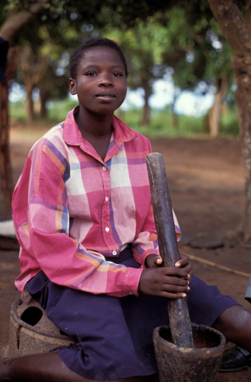 Pounding the Meal in Zambia — Woman in Zambia pauses for camera, as she pounds her cornmeal in the old traditional way. — Zambia, Africa, Woman, pounding stick