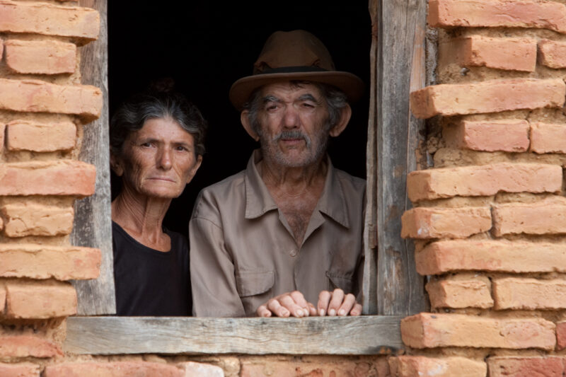 Living in Poverty — Elderly couple living in a desert region of Brazil look out the window of their home. — Brazil, South America, faces, poverty, poor