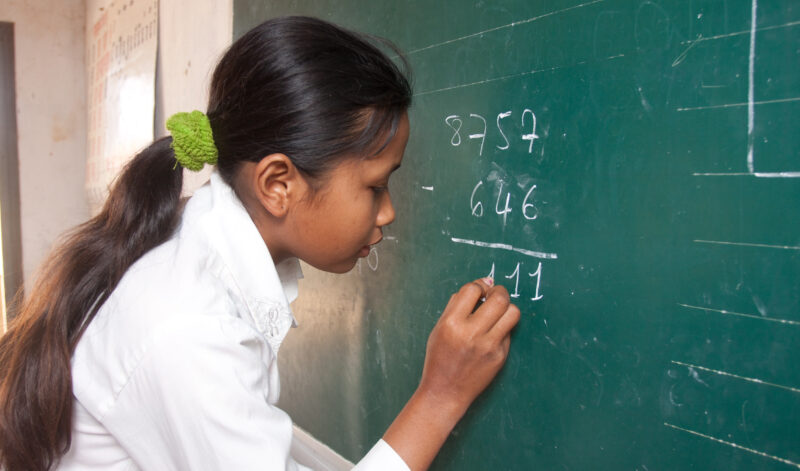 Girl Does math on the Board — Stock image of young girl in Cambodia doing a math problem on the board at her school — Cambodia, ADRA, children, girls, education