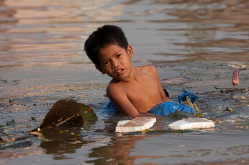 Children of Cambodia — Boy pulls bag of trash out of the river to see if there is anything valuable. — Cambodia, faces, child, children, poor