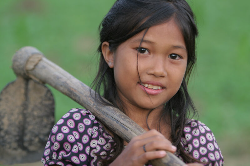 Girl with Hoe in Cambodia — Girl walks out to field to help her parents weed the family garden — Cambodia, faces, child, children, poor