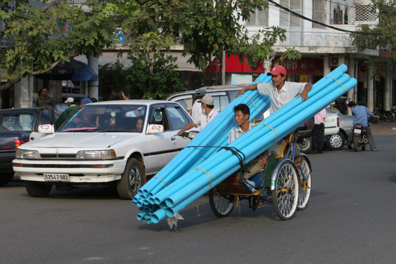 Cyclo Driver in Cambodia — Stock image of cyclo driver working the streets of Phnom Penh, Cambodia: delivering plastic water pipes. — Cambodia, street, stree...