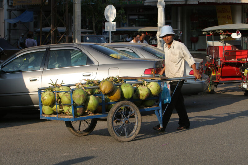 Selling Coconuts in Cambodia — Man walks the streets of Phnom Penh trying to make a little money selling coconuts. — Cambodia, street, streets, traffic, Phno...