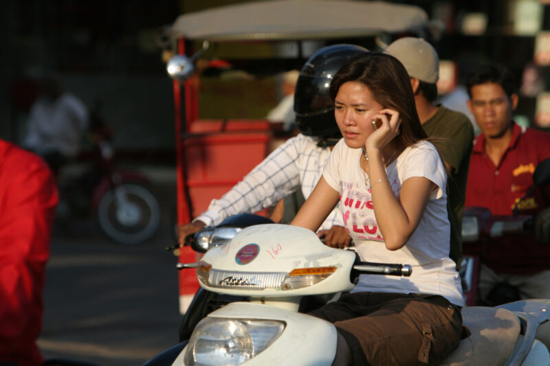Talking while Driving in Cambodia — Woman talks on her phone while driving her motor scooter in Phnom Penh, Cambodia — Cambodia, street, streets, traffic, mo...