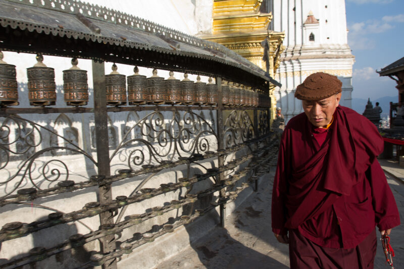 Buddhist Monk in Nepal — Stock Image of Buddhism: Buddhist monk walks by prayer wheels at the Swayambhunath Stupa in Kathmandu — Nepal, contains, Monk, and, ...