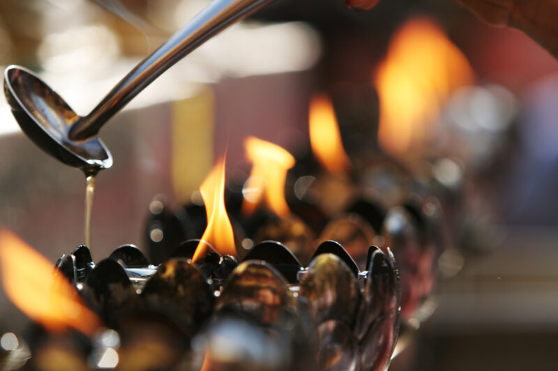 Feeding the Flame at the Temple — Stock images of Buddhism, symbols of Buddhism: Closeup of pouring oil into a burning flame at a Pagoda in Chiang Mai, Thail...