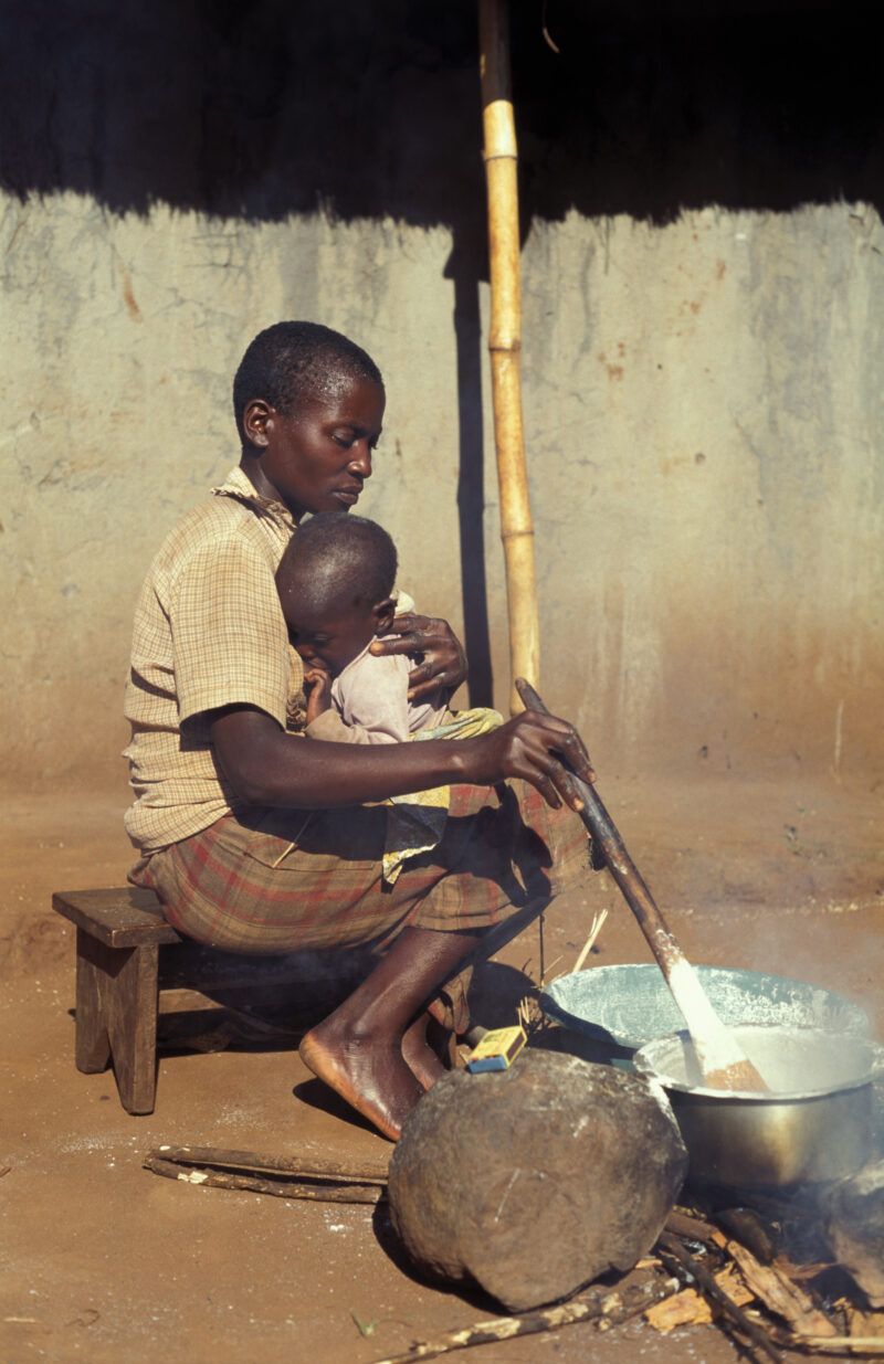 Cooking the Meal in Malawi — Woman cooks over an open fire in front of her home in Malawi, with baby on her back — Malawi, Africa, Food Security, food, proce...