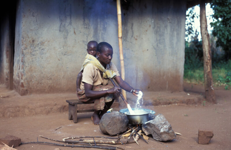 Cooking the Meal in Malawi — Woman cooks over an open fire in front of her home in Malawi, with baby on her back — Malawi, Africa, Food Security, food, proce...