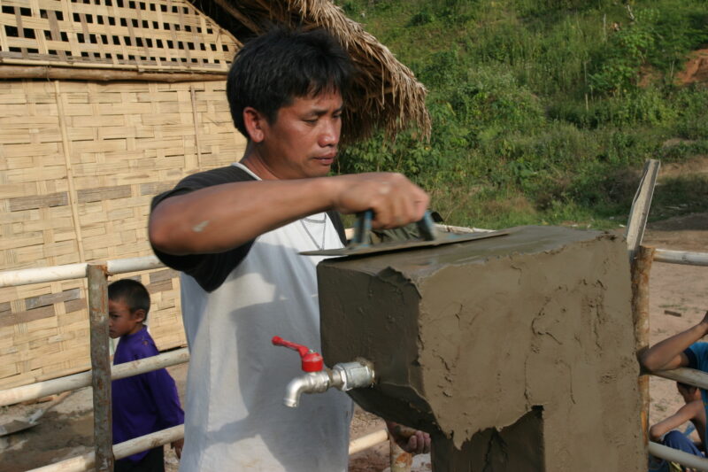 Installing the Tap in Laos — ADRA worker puts the final touches on a water tap, one of many scatered through out the village as part of a gravity fed water s...