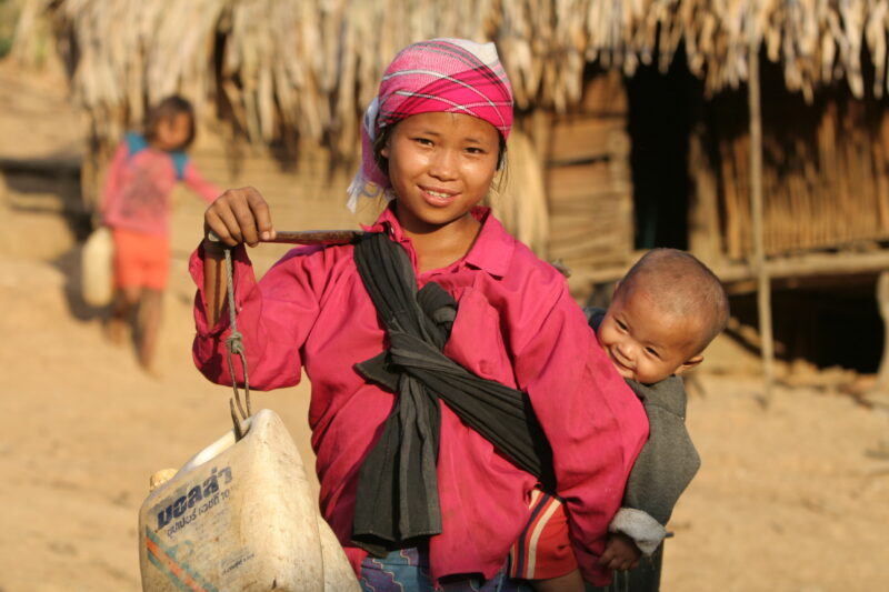 Collecting Water in Laos — Stock image of girl with baby on her back, collecting water from the new water system in her village in Laos. — Laos, ADRA, ADRA C...