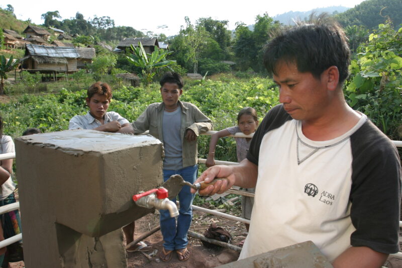 Installing the Tap in Laos — ADRA worker puts the final touches on a water tap, one of many scatered through out the village as part of a gravity fed water s...