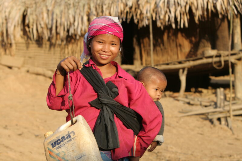 Collecting Water in Laos — Stock image of girl with baby on her back, collecting water from the new water system in her village in Laos. — Laos, ADRA, ADRA C...