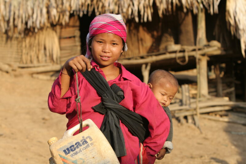 Collecting Water in Laos — Stock image of girl with baby on her back, collecting water from the new water system in her village in Laos. — Laos, ADRA, ADRA C...
