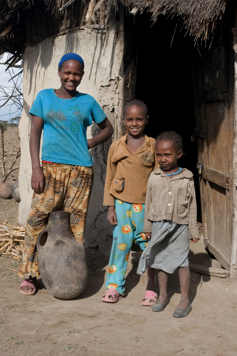 Children in Rural Africa — Poor children of Ethiopia stand outside the doorway to their mud hut, with water container — Ethiopia, Africa, African, Africans, ...