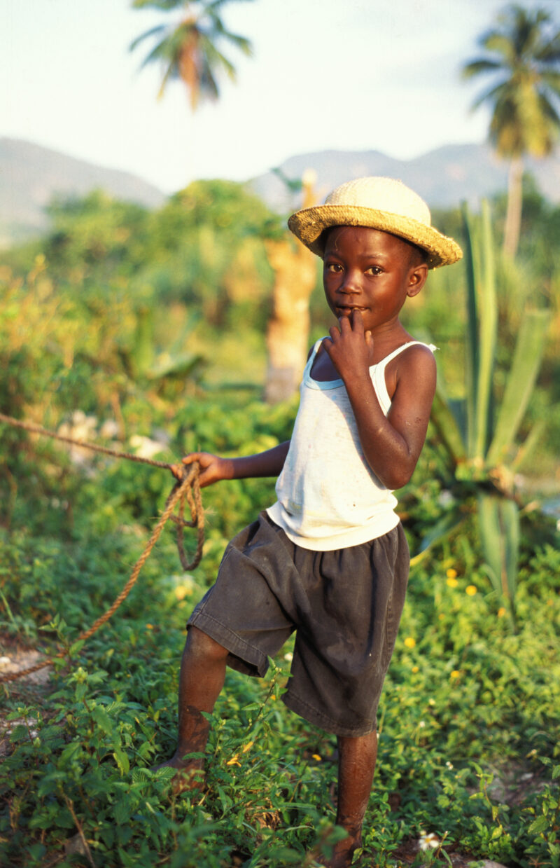 Stock Images of Haiti — Stock Image of Haiti: Boy holding the rope to his goat with a straw hat — Haiti, Haitian, boy, boys, hat