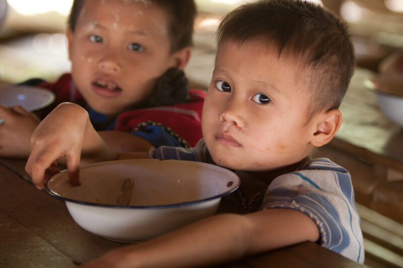 Getting a Hot Meal at School — Children eat a bowl of hot soup, as part of their school feeding program, at a Karen refugee camp, near the Thai border with M...