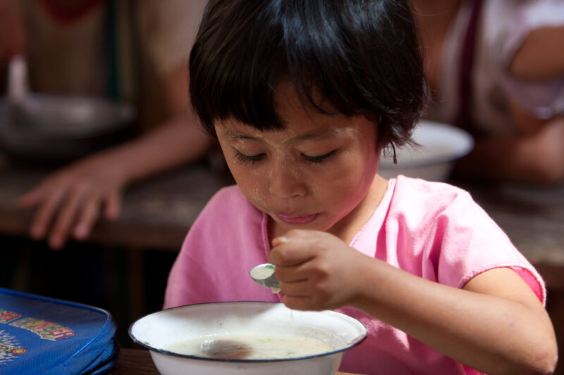 Getting a Hot Meal at School — Children eat a bowl of hot soup, as part of their school feeding program, at a Karen refugee camp, near the Thai border with M...