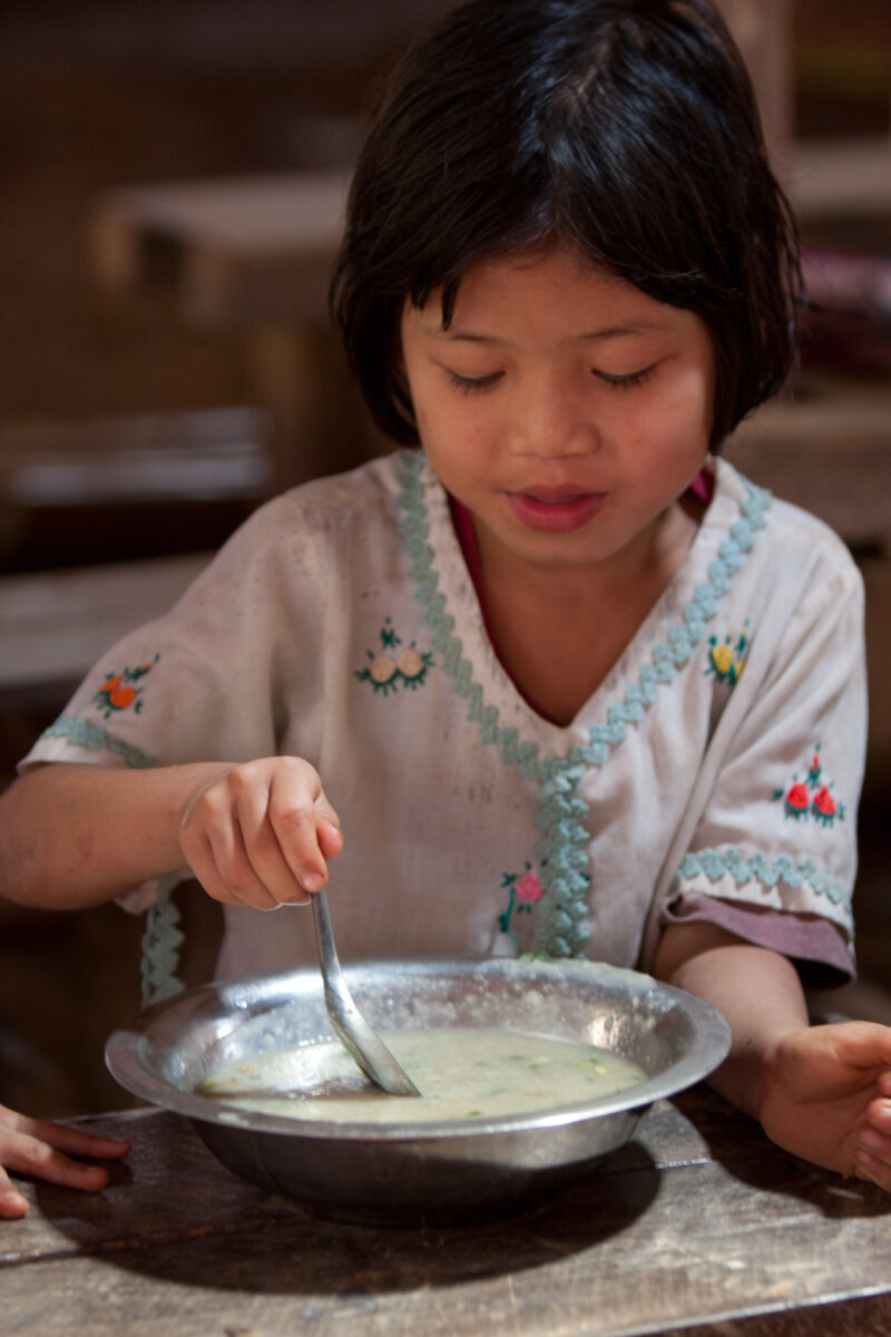 Getting a Hot Meal at School — Children eat a bowl of hot soup, as part of their school feeding program, at a Karen refugee camp, near the Thai border with M...