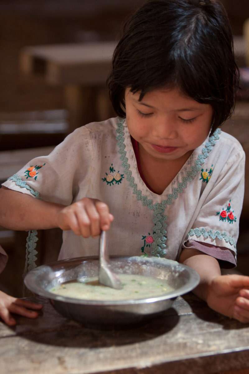 Getting a Hot Meal at School — Children eat a bowl of hot soup, as part of their school feeding program, at a Karen refugee camp, near the Thai border with M...