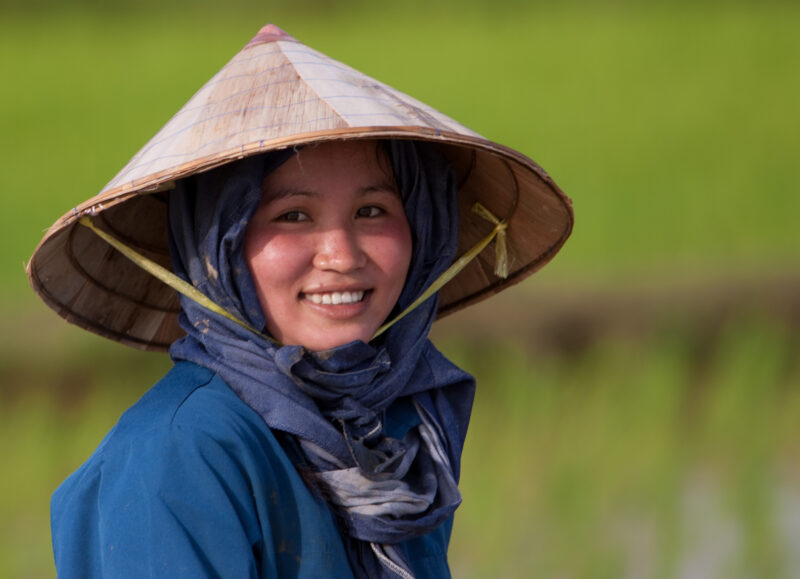 Woman Smiles in Laos — Beautiful young woman in bamboo cone hat, pauses from her work in planting rice, to smile and pose for camera. — Laos, Southeast Asia,...