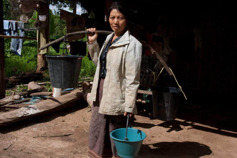 Collecting Water in Laos — Woman heads to the pump for water, with all her pails. — Laos, Southeast Asia, woman, water, collecting water