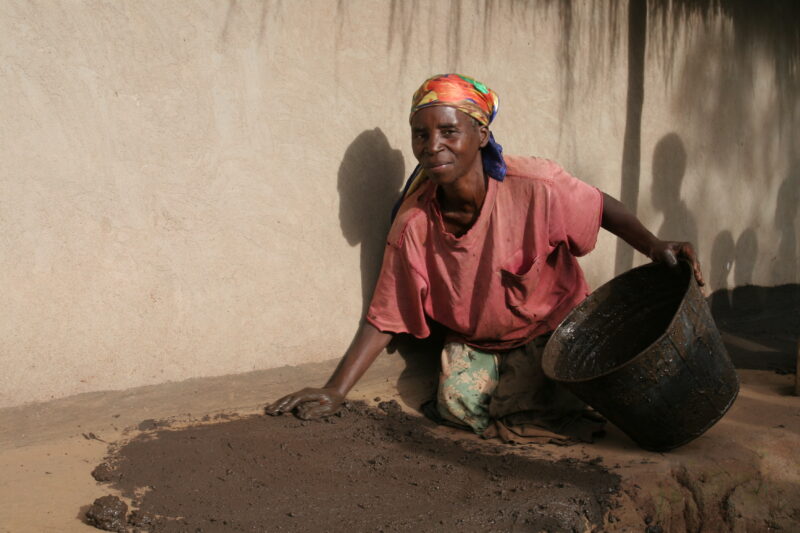 Woman with Mud Mixture — Woman coats her house Veranda with a mud mixed with plants that repel misquitos. — Malawi, Africa, woman, women, mud