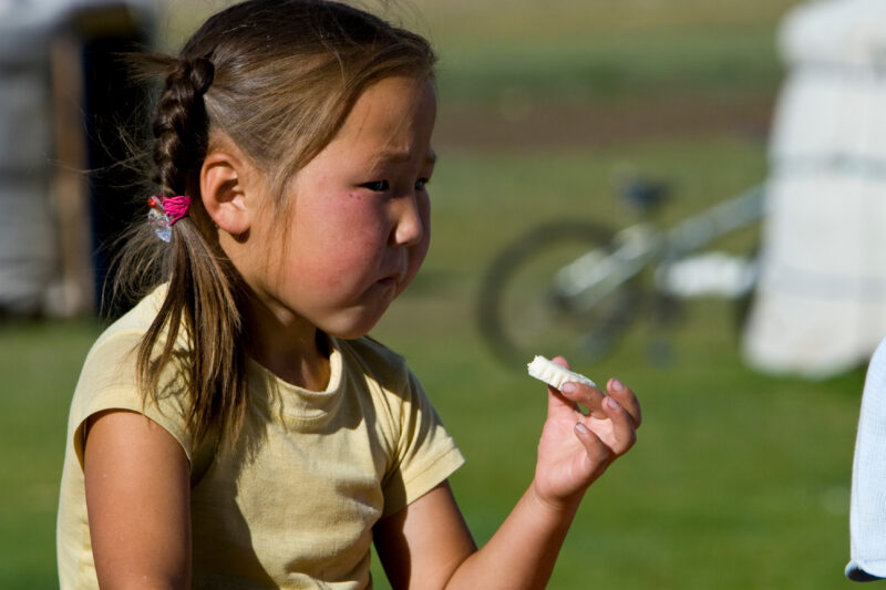 Girl Eats Milk Cake in Mongolia — Stock Images of life in Rural Mongolia, and the people who live there: Young girl eats — Children, Faces, Mongolia, eating,...