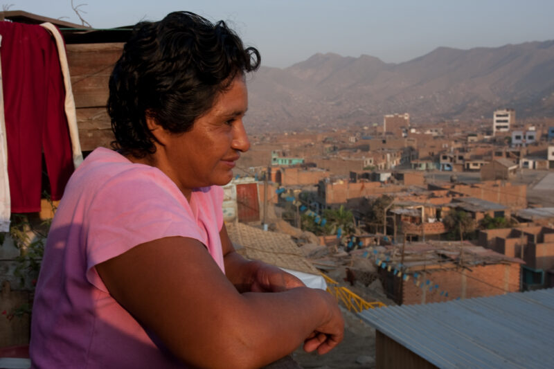A view of Poverty — Profile of a mother and her two children living in one of the poor communities on the outskirts of Lima, Peru: Woman stands on the porch ...