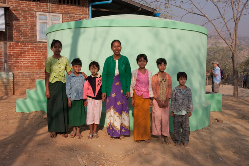 Water Tank in Myanmar — Children and teacher stand in front of the water tank at their school, that collects rain water from the roof of the classrooms, in a...