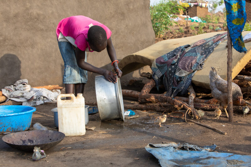 Washing Dishes — Young refugee girl washes dishes in her new home in Uganda. — Person, Refugee, Refugee Settlement, South Sudan