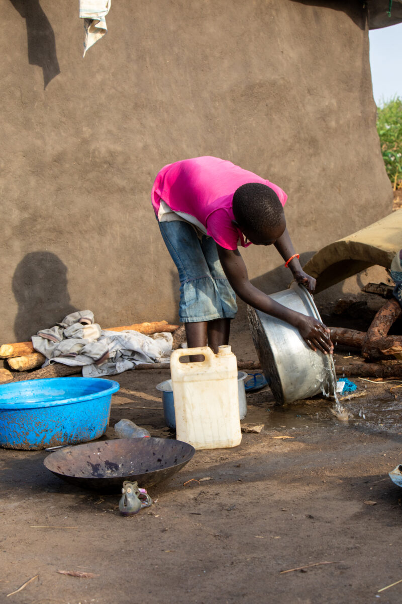 Washing Dishes — Young refugee girl washes dishes in her new home in Uganda. — Person, Refugee, Refugee Settlement, South Sudan