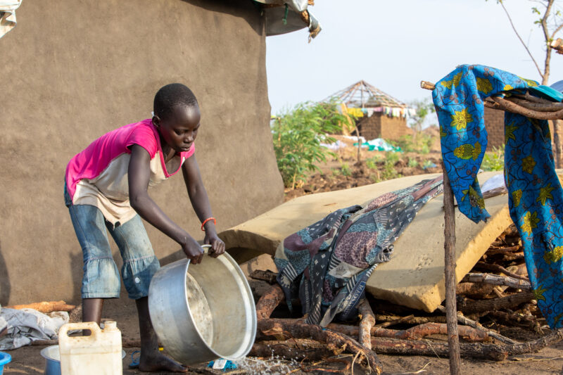 Washing Dishes — Young refugee girl washes dishes in her new home in Uganda. — Child, Eyes Closed, Female, Frontal Face, One Face