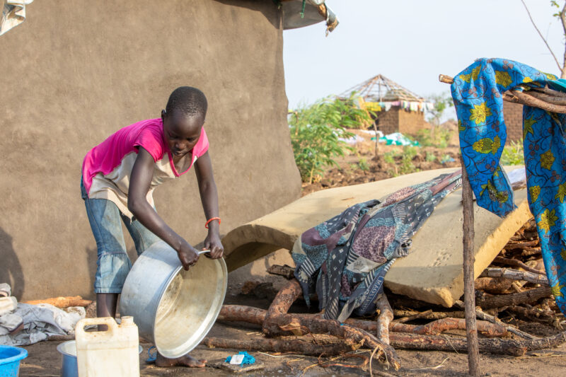Washing Dishes — Young refugee girl washes dishes in her new home in Uganda. — Person, Refugee, Refugee Settlement, South Sudan