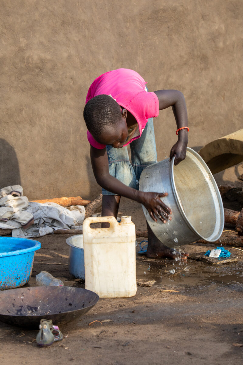 Washing Dishes — Young refugee girl washes dishes in her new home in Uganda. — Person, Refugee, Refugee Settlement, South Sudan