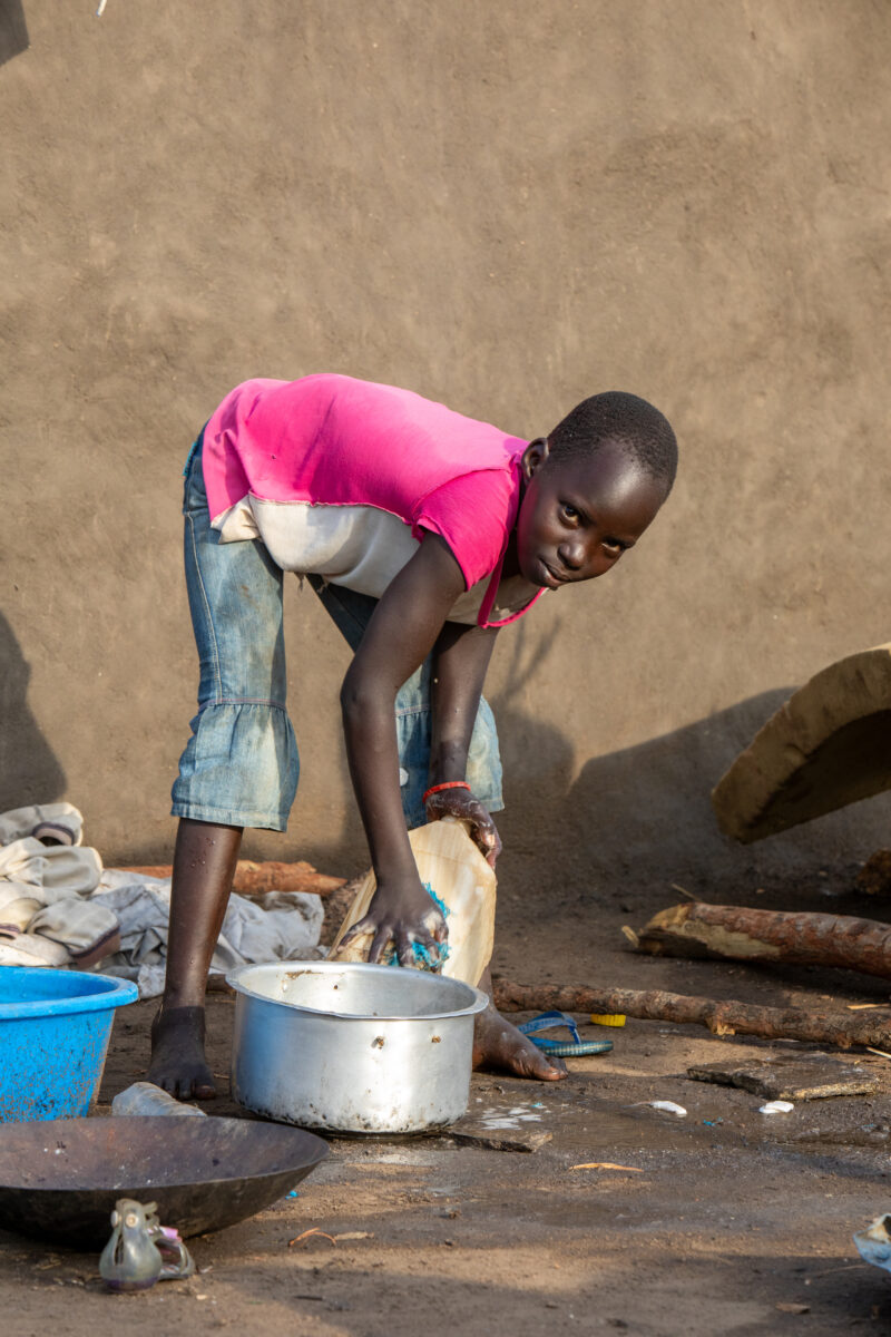 Washing Dishes — Young refugee girl washes dishes in her new home in Uganda. — Eyes Open, Female, Frontal Face, One Face, Person