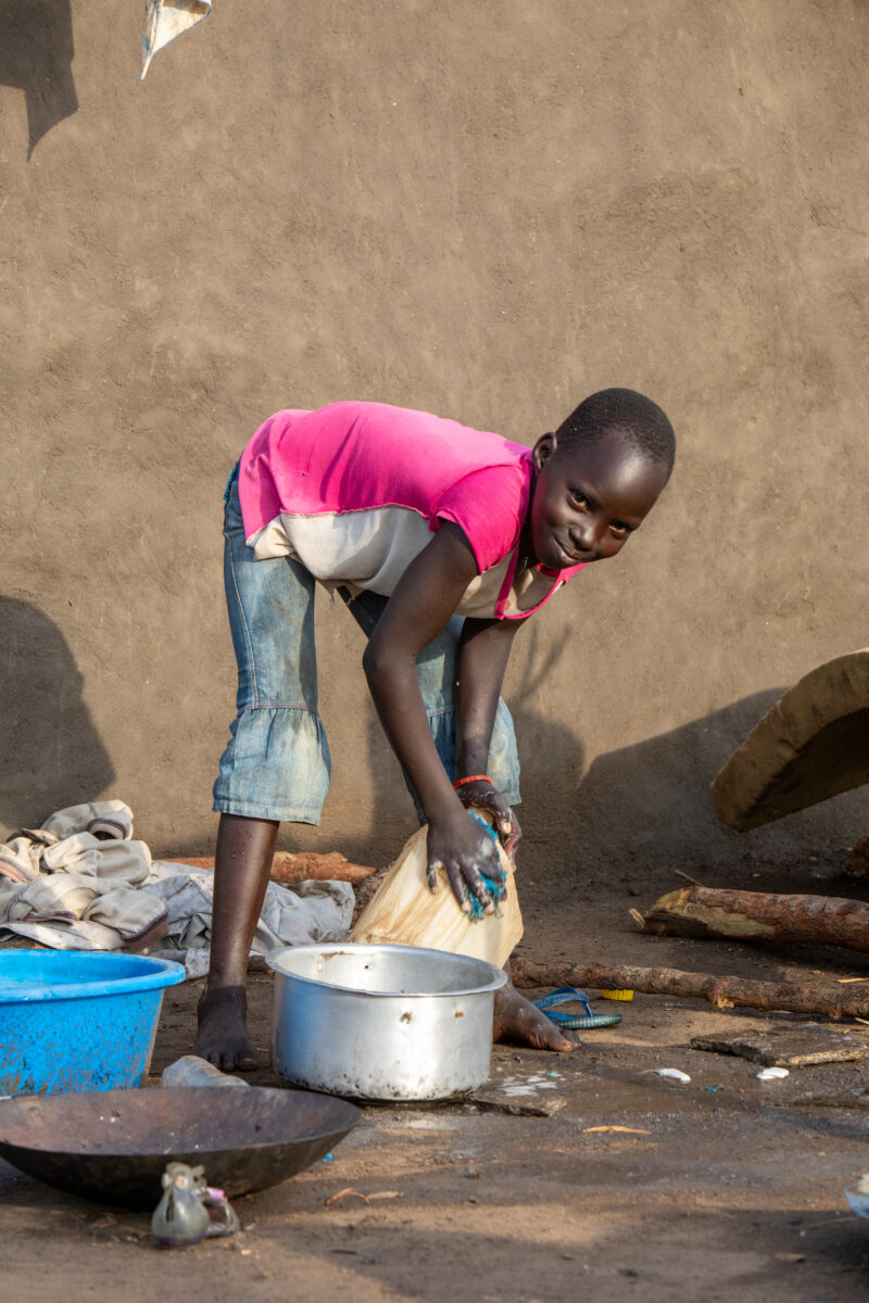 Washing Dishes — Young refugee girl washes dishes in her new home in Uganda. — Child, Eyes Open, Female, Frontal Face, One Face
