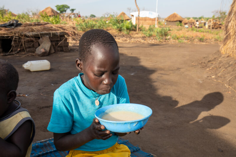 Refugee Child Eating — Refugee from South Sudan takes a morning meal of porridge — Child, Eyes Closed, Frontal Face, Male, One Face