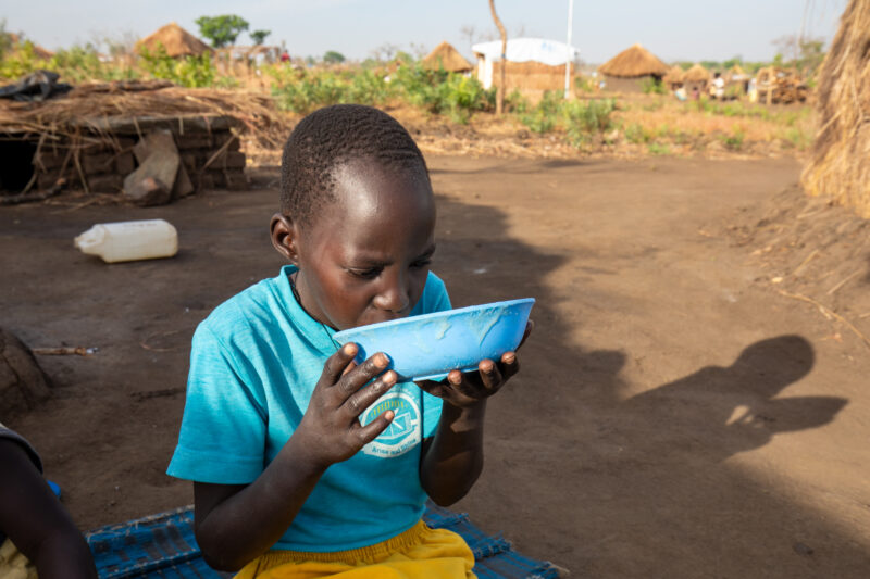 Refugee Child Eating — Refugee from South Sudan takes a morning meal of porridge — One Face, Person, Portrait, Profile Face, Refugee