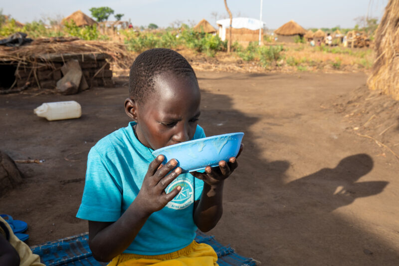 Refugee Child Eating — Refugee from South Sudan takes a morning meal of porridge — One Face, Person, Portrait, Profile Face, Refugee