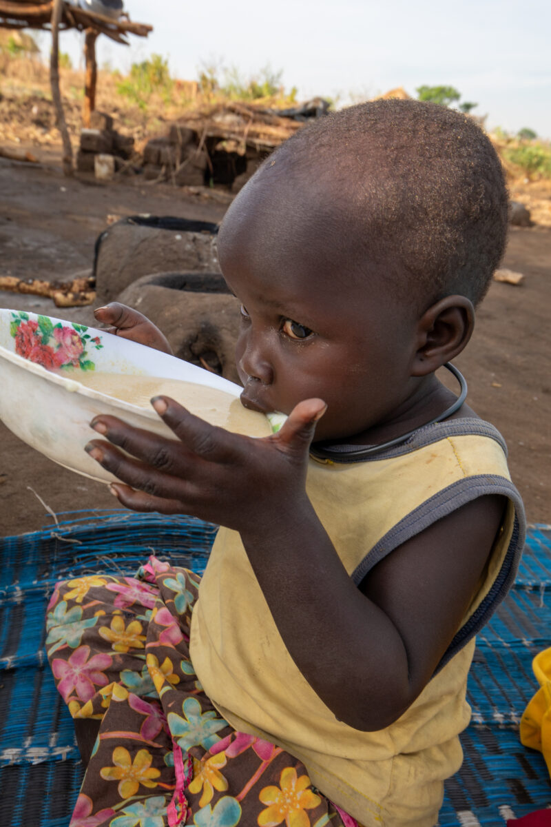 Refugee Child Eating — Refugee from South Sudan takes a morning meal of porridge — One Face, Person, Portrait, Profile Face, Refugee