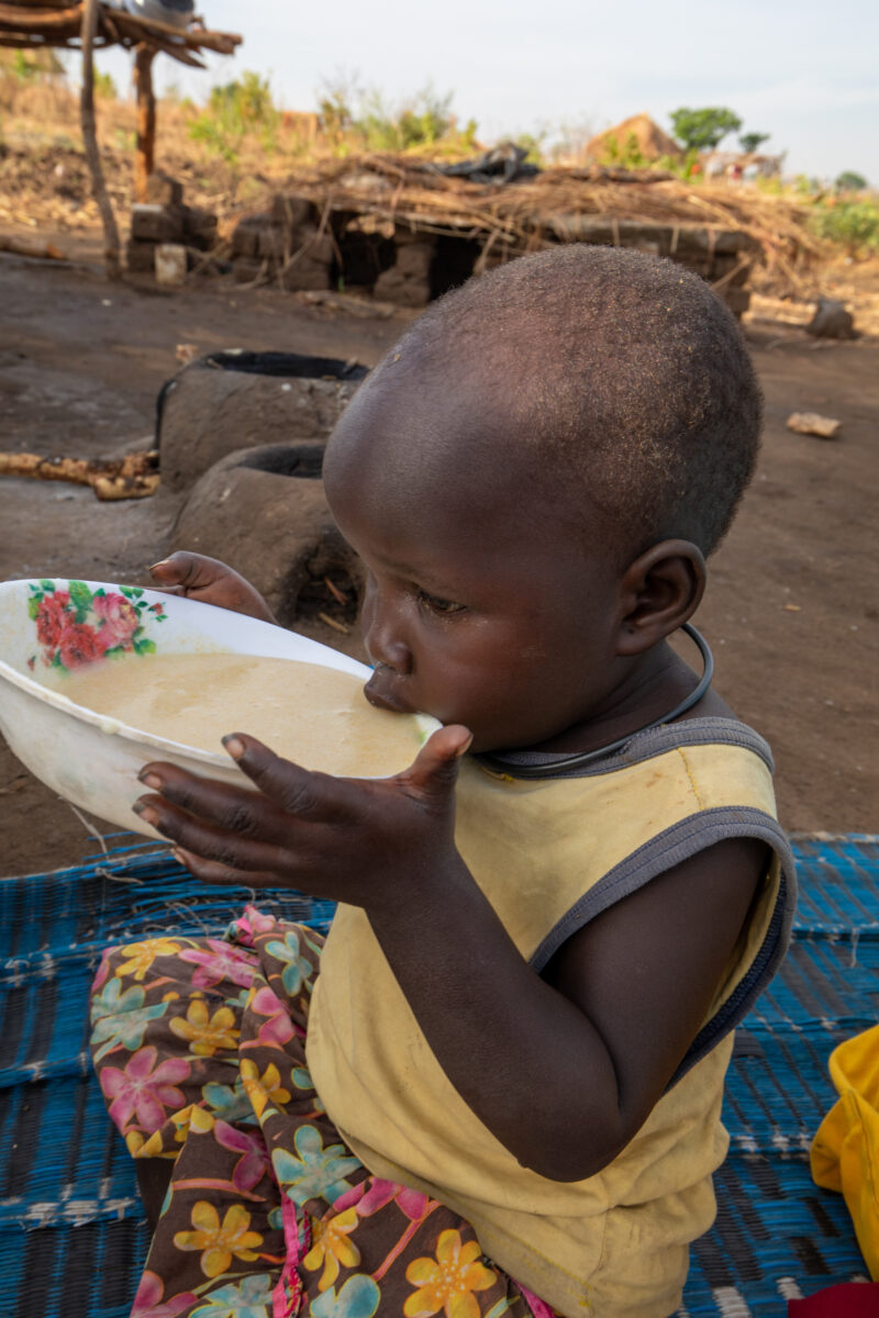 Refugee Child Eating — Refugee from South Sudan takes a morning meal of porridge — One Face, Person, Portrait, Profile Face, Refugee