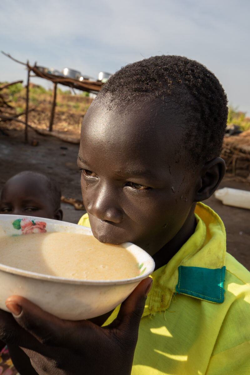 Refugee Child Eating — Refugee from South Sudan takes a morning meal of porridge — Food, Frontal Face, Male, Person, Profile Face