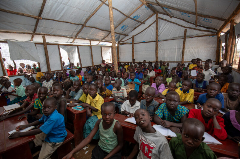 School in the Refugee Settlement — Refugee Children attend school at the refugee settlement they call their new home. — Adult, Child, Eyes Open, Female, Fron...