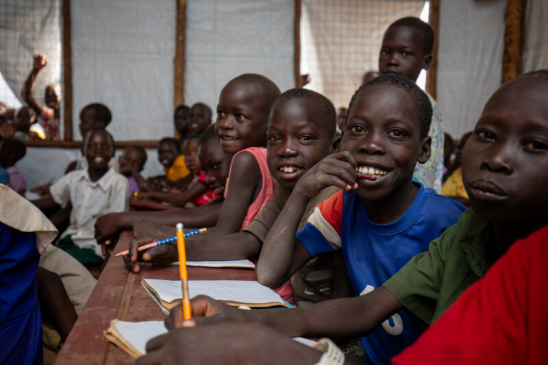 School in the Refugee Settlement — Refugee Children attend school at the refugee settlement they call their new home. — Adult, Child, Eyes Open, Female, Fron...