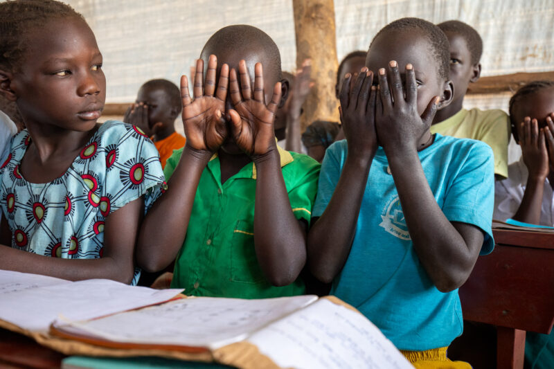 School in the Refugee Settlement — Refugee Children attend school at the refugee settlement they call their new home. — Adult, Eyes Open, Female, Frontal Fac...