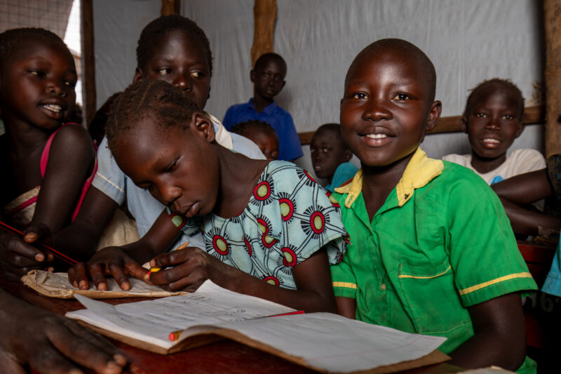School in the Refugee Settlement — Refugee Children attend school at the refugee settlement they call their new home. — Adult, Beard, Eyes Open, Female, Fron...