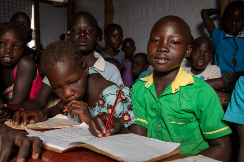 School in the Refugee Settlement — Refugee Children attend school at the refugee settlement they call their new home. — Adult, Child, Eyes Open, Female, Fron...