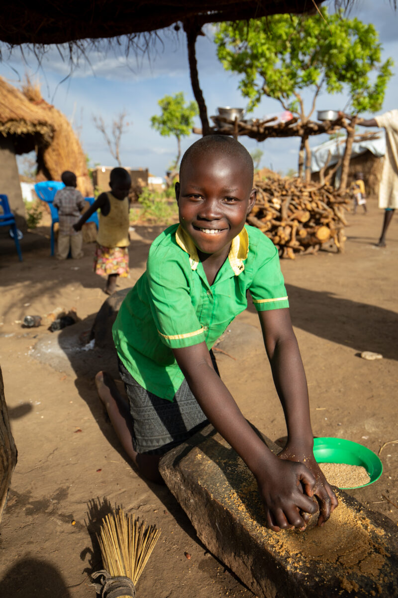 Grinding the Meal — Refugee girl grinds grain on a grinding stone. — Child, Eyes Open, Frontal Face, Male, One Face