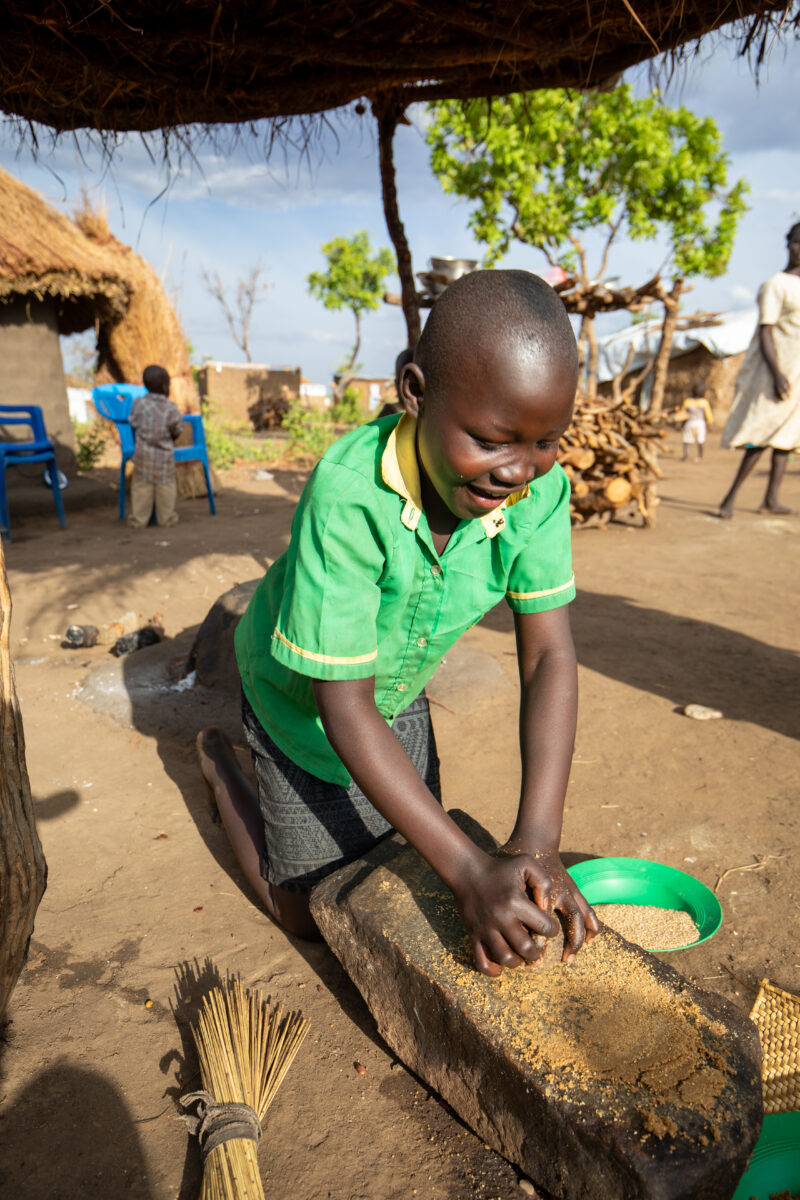 Grinding the Meal — Refugee girl grinds grain on a grinding stone. — Baby, Eyes Closed, Frontal Face, One Face, Person