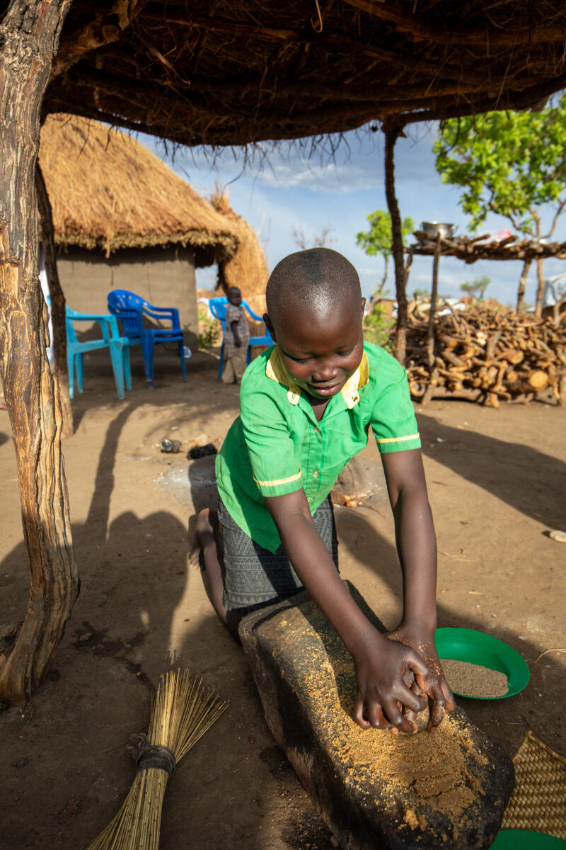 Grinding the Meal — Refugee girl grinds grain on a grinding stone. — Baby, Eyes Closed, Frontal Face, One Face, Person